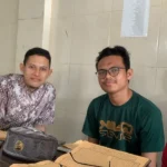 Tiga pemuda duduk mengelilingi meja kayu dengan kitab kuning terbuka dan sebuah peci di atasnya