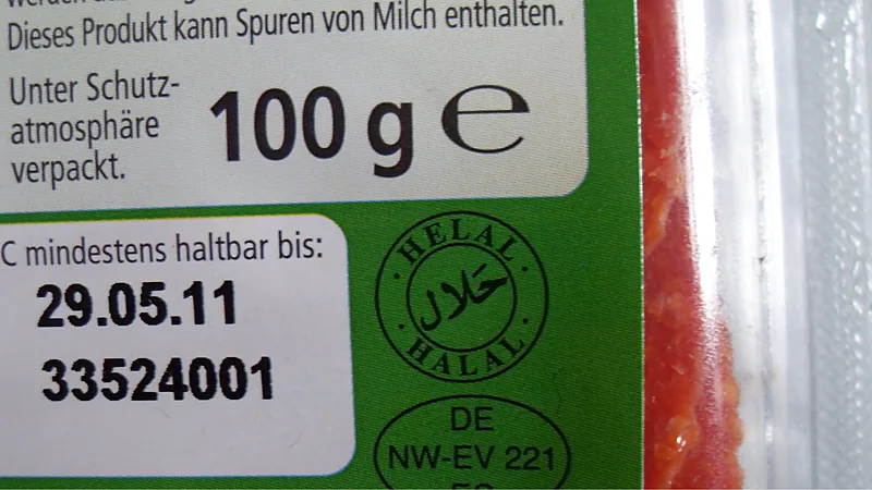 Logo halal lembaga luar negeri pada kemasan salami Jerman Kemasan salami buatan Jerman dengan stempel bundar bertulisan HELAL dan HALAL beserta kaligrafi Arab, di sebelah tanggal kedaluwarsa dan berat bersih 100 gram