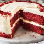 Kue red velvet berlapis krim putih yang sudah dipotong di atas piring marmer