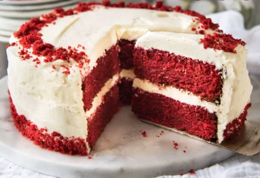 Kue red velvet berlapis krim putih yang sudah dipotong di atas piring marmer