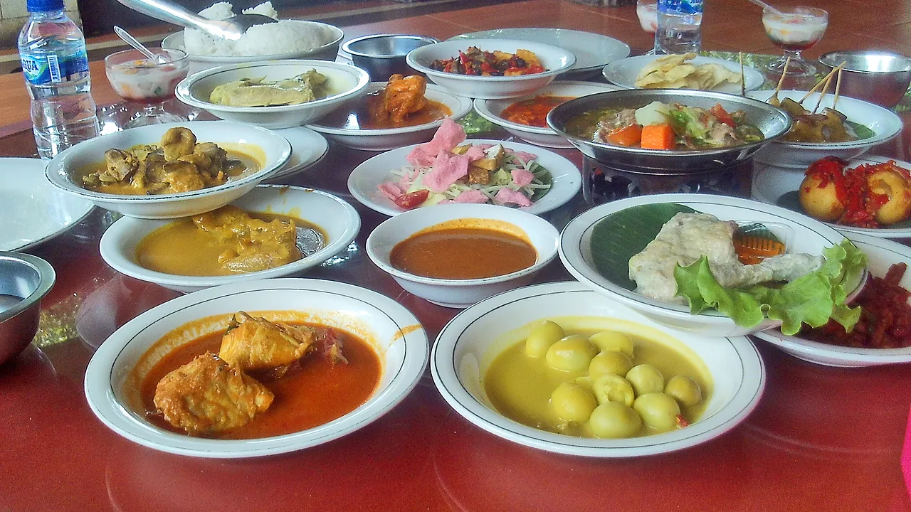 Belasan piring lauk masakan Padang tersaji di meja merah: gulai ayam, rendang, ikan goreng, dan telur berkuah kuning