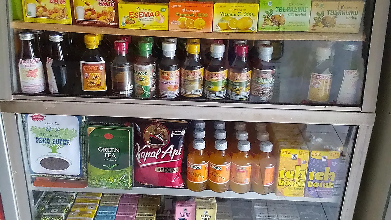 Rak kaca sebuah warung di Kebumen berisi jamu kemasan, madu botolan, vitamin C sachet, teh, kopi, dan susu kotak