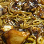 Jajangmyeon dari dekat: mi kuning tebal berbalut saus pasta kacang hitam bersama potongan daging, bawang bombai, dan kentang
