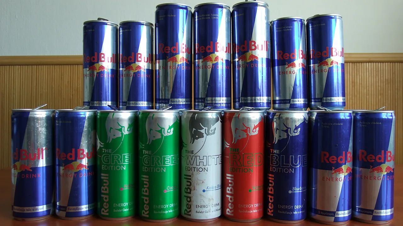 Dua baris kaleng Red Bull berdiri rapat, kaleng biru perak reguler di belakang dan varian Green, White, Red, serta Blue Edition di depan